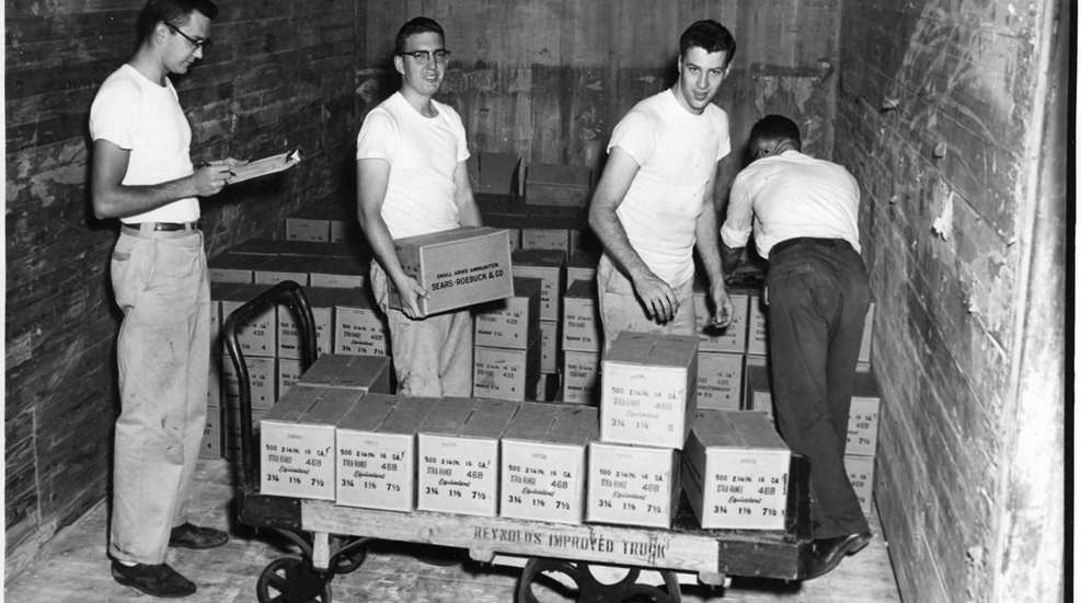 black & white archival photo of five young men in approx. 1950s loading shotshells into boxes