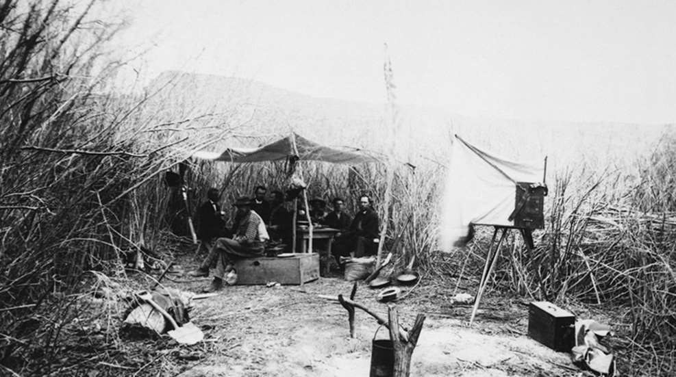 historical photo of Powell seated in front of makeshift tent