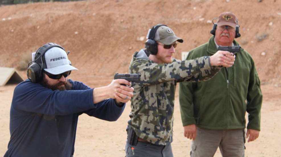 two men shoot handguns as instructor watches