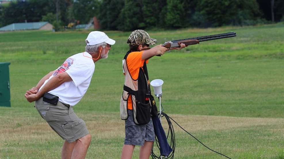 young shotgunner takes aim with instructor watching carefully