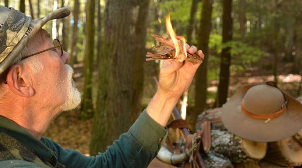 Man blows on flaming kindling to ignite it