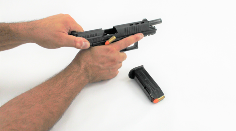 hand holding slide back of pistol as dummy round is expelled
