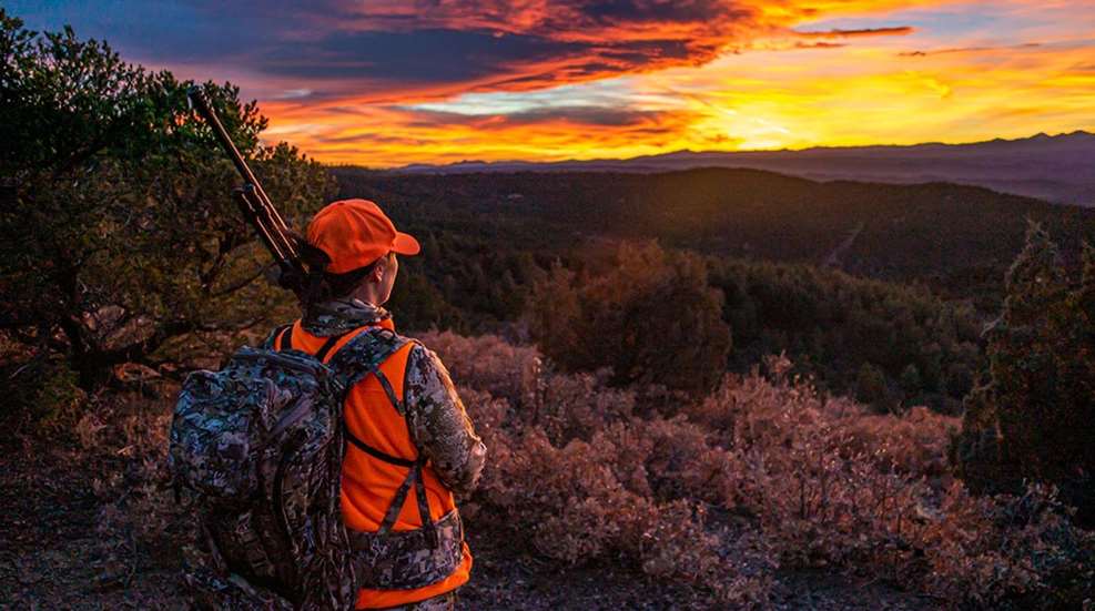 Huntress on mountainside gazing at sunset