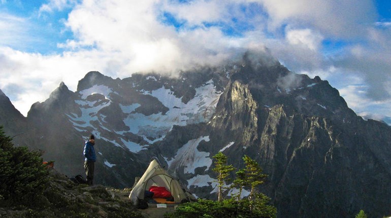lone camper perched with alpine tent on mountain crag