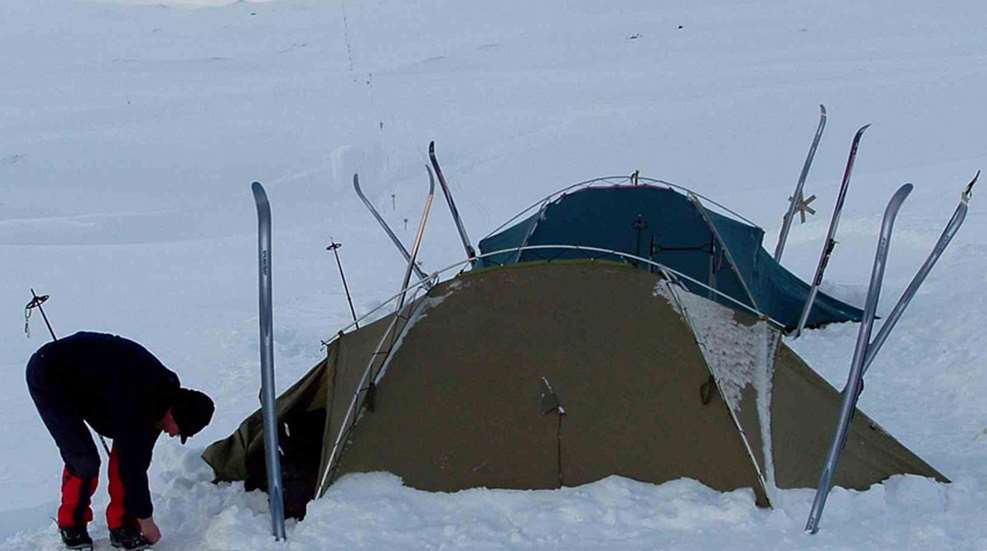person erecting a mountaineer tent in the snow