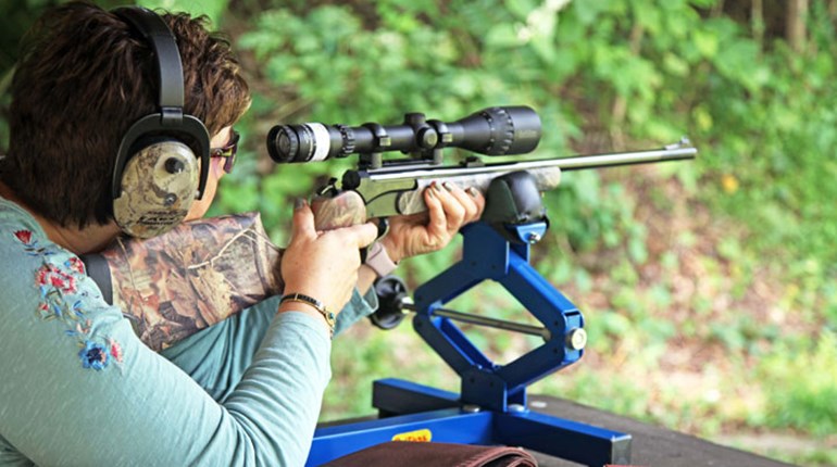 Woman squeezing rifle's trigger from benchrest 